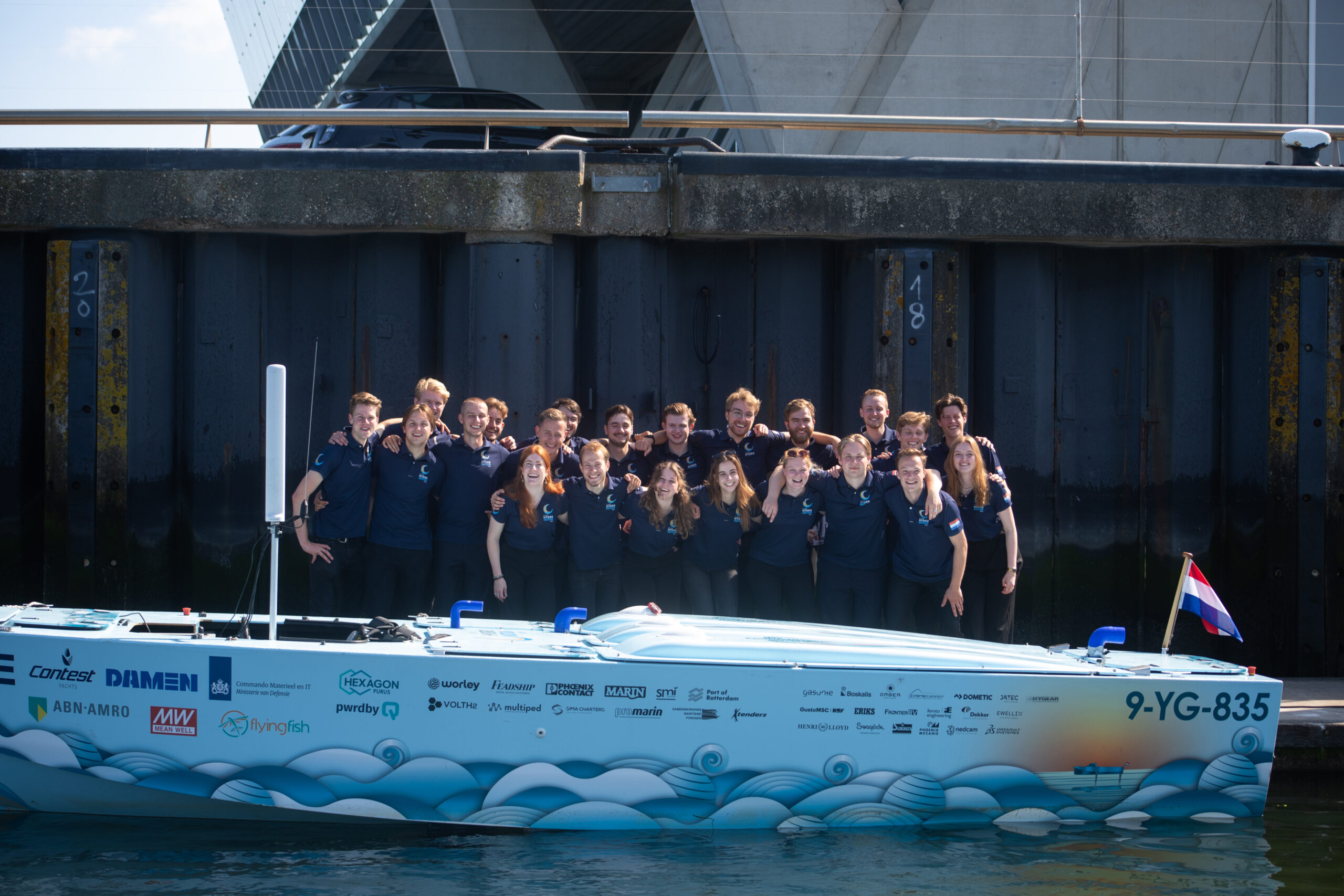 TU Delft Hydro Motion team standing beside their hydrogen-powered boat at the water’s edge, preparing for the North Sea crossing competition.