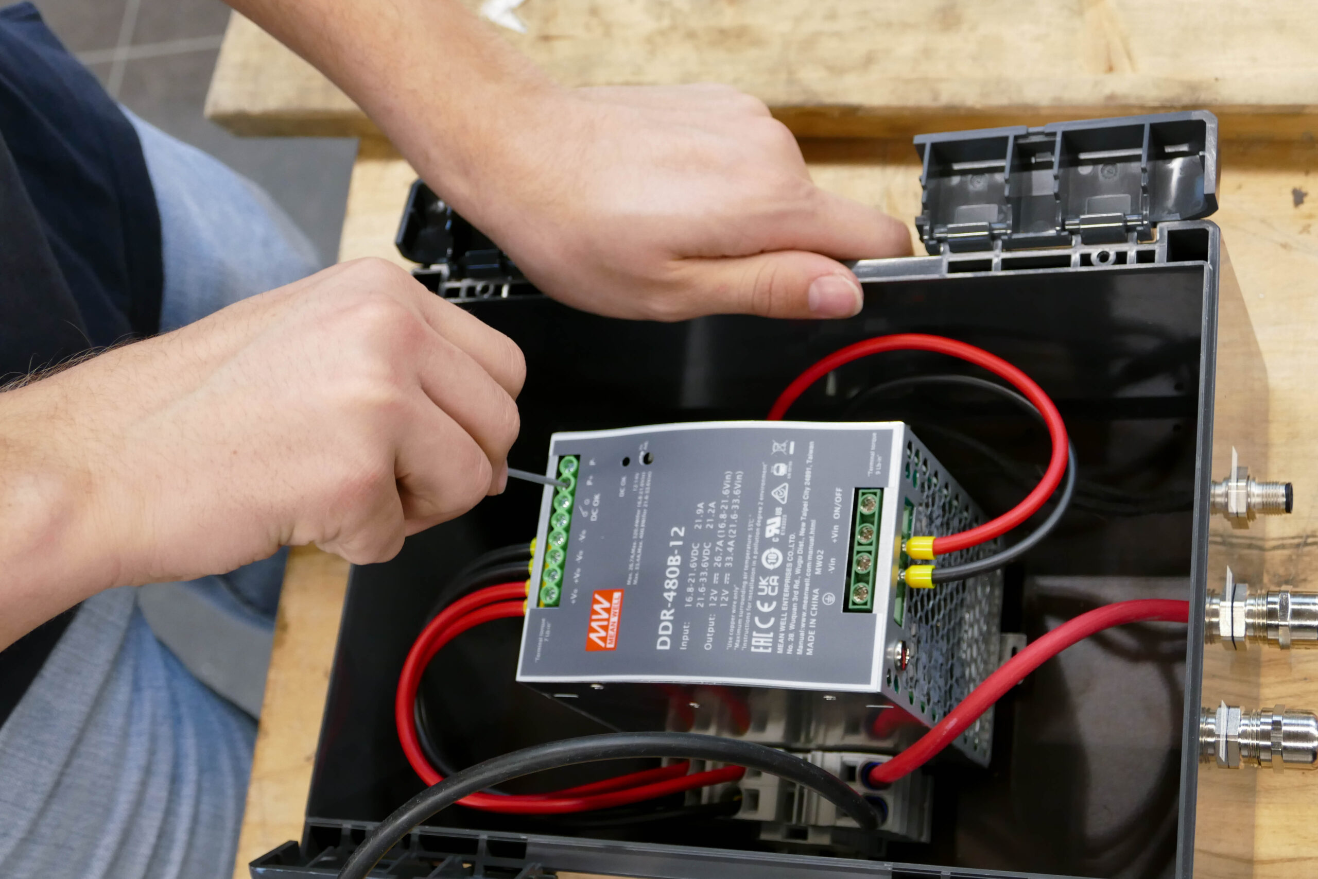 A TU Delft student securing a DDR-480B-12 DC-DC converter inside a protective enclosure during the hydrogen-powered boat project.