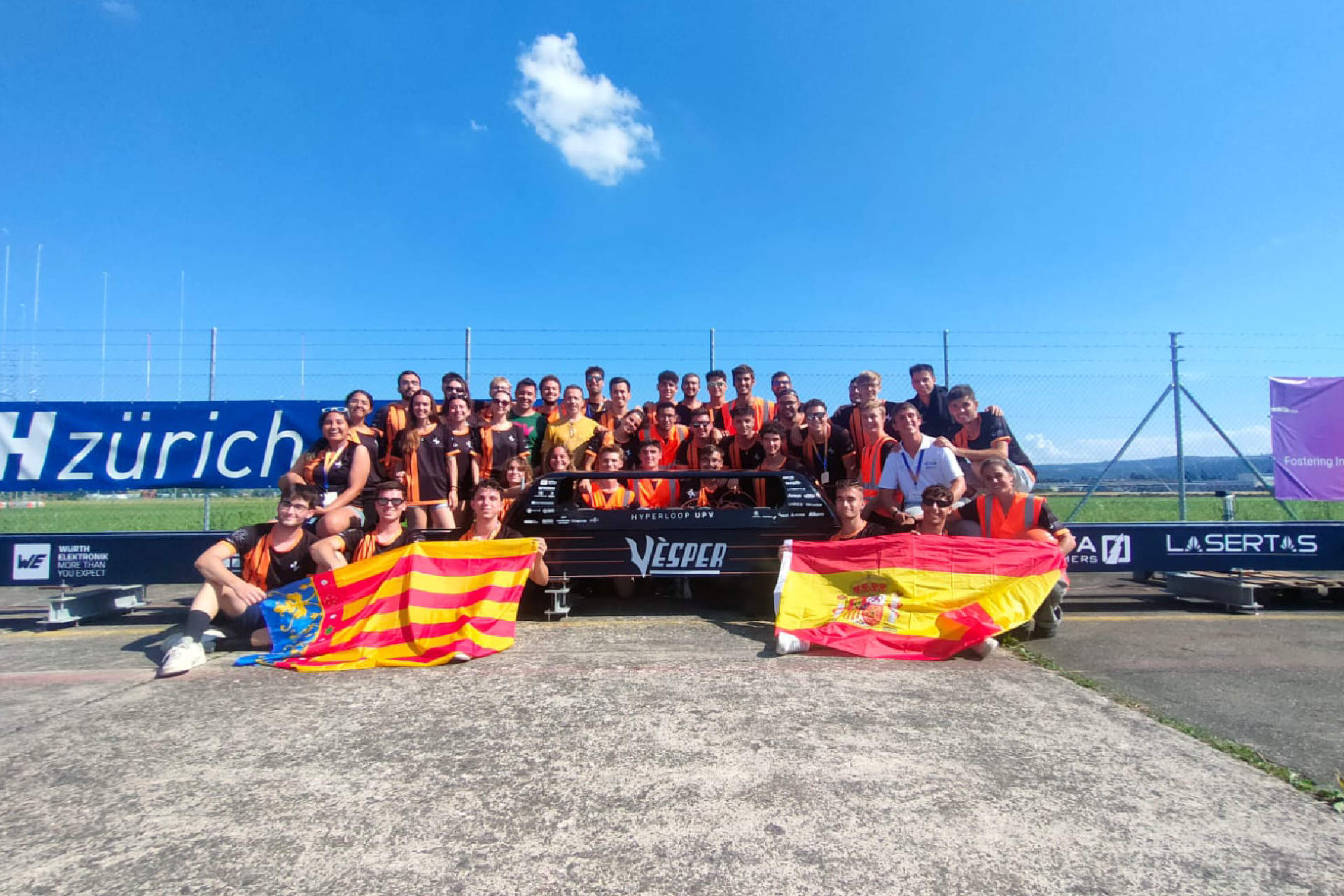 Hyperloop UPV team posing for a group photo at the competition venue, proudly holding their flags after showcasing their MEAN WELL-powered Hyperloop vehicle.